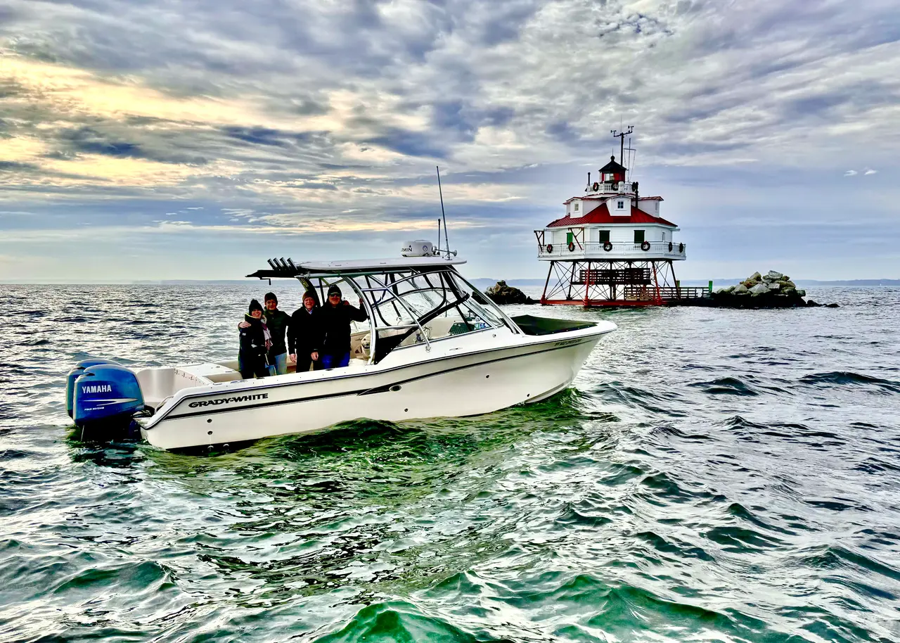A Grady-White alongside Thomas Point Shoal Light on the Chesapeake, under a broken sky